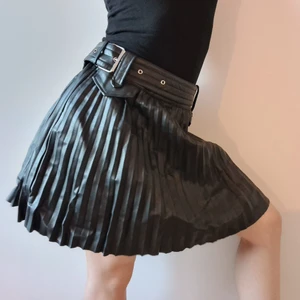 Svart pliserad kjol skinnimitstion, stl 38 - Tuff, svart, pliserad kjol i skinnimitation med bälte. Size 10 / stl 38. Märke: River Island. Dragkedja på sidan, se sista bilden. Fuskfickor framtill. Fraktkostnad tillkommer. Endast swishbetalning.