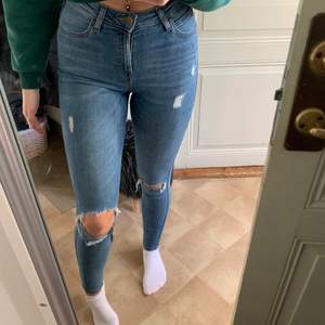 Lee-jeans i en blå tvätt med slitningar, stretchigt material och hellånga, är 176 cm