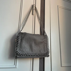 beige axelremsväska  - Beige väska med silverkedja från Tiamo. Finns flera fack inuti och på baksidan av väskan. Användes mycket i somras men är fortfarande i bra skick. Frakt tillkommer. 