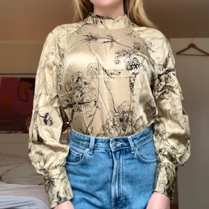 Mönstrad blus med ståkrage - Beige blus i siden/satinliknande material med mönster och ståkrage. Den är fantastisk men tyvärr bara använd en gång så i perfekt skick! Från H&M, strl S men passar även XS & M. Knappar på ärmarna och där bak vid kragen.