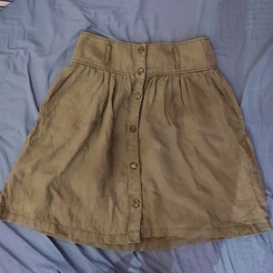 Grön kjol - En grön kjol med knäppning fram och plats för bälte. Kjolens midja är 38 cm och är 50 cm lång.