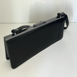 Liten svart handväska - Väldigt enkel svart väska med silverdetaljer och knäpplås. Ett litet fack inuti med dragkedja och rymmer mobil och kort, lagom för en utekväll. Svårt att visa storlek på väskan men bara att fråga annars! Höjd:11cm, Bredd:23cm, Botten: 5 cm, Remmen: 45 cm 