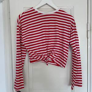 Snygg vit/röd randig croppad tröja med lite vida armar och knytning i midjan. Bra skick, använd sparsamt. Spårbar frakt med DHL inräknat i priset!!
