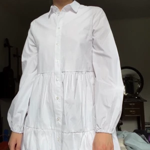 Vit skjortklänning  - Säljer denna skjortklänning från Stradivarius då den är för kort för mig (jag är 167cm och den slutar någon centimeter under rumpan). Superfin med sina långa armar och lite tjockare material som gör att den inte är genomskinlig alls! Perfekt på sommaren som den är eller nu på hösten med en stickad tröja till. Aldrig använd med lapparna kvar! 