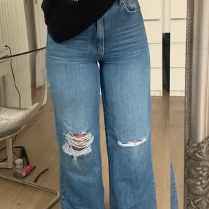 Blå raka jeans - Säljer dessa blå jeans som har en bra passform i midjan samtidigt som dem har en lös passform på benen. Jeansen är köpta på Ginatricot. På knäna är de hål/slitningar. De är i gott skick och har använts vid 1-2 tillfällen. Jag säljer dem eftersom de inte kommit till användning