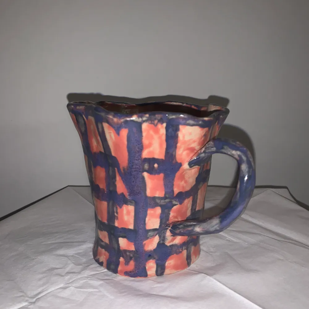 En handgjord kopp i keramik, koppen är rosa med lila rutor samt ett lila öra. . Övrigt.