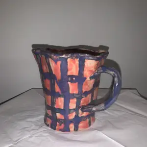En handgjord kopp i keramik, koppen är rosa med lila rutor samt ett lila öra. 