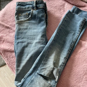 Jeans - Blå lågmidjade jeans från bikbok i storlek xs. Hål på ena knät och snyggt avklippta vid fötterna. Sitter supersnyggt på.