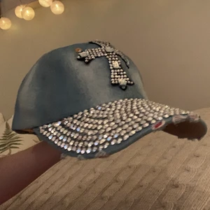 Denim keps med kors på - Blå jeans keps med rhinestones på och ett kors av rhinestones. Den är riven längst fram med rosa under.