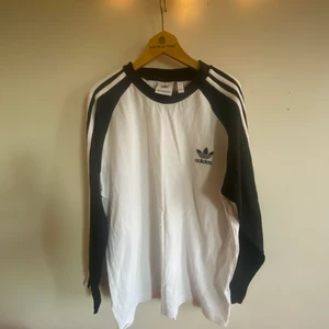 Långärmad Adidas tröja  - Tunn tröja från Adidas, gråvit med svarta armar i storlek large.  Perfekt på sommarkvällar   Kör garderobsrensning och har egentligens vårt att slita mig från den. Men måste göra mig av med saker, så först till kvarn får köpa :)