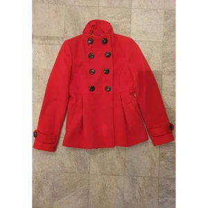 Röd kort kappa M - Super snygg röd kappa i M. Den är inte så tunn, så den passar perfekt för kallare vårdagar 🌸 Den går in vid midjan så man får en fin silhouette. Man kan bära kragen på två olika sätt, antingen uppknäppt hela vägen eller halv öppen. Den är köpt i Italien och den är sparsamt använt. Man kan ha den över en klänning eller med jeans, passar allt! 😍 Den har också fickor men dem är fortfarande ihopsydda. 