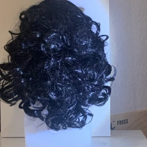 Peruk svart kort krulligt  - Peruk som är kort, fint svart hår. Enkel att sätta på, du står för frakt och får med påse för ditt hår att lägga in det i. Hör av dig för mer info.