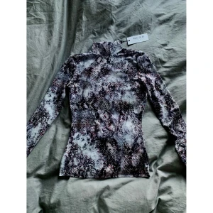 Meshtröja från NAKD - Aldrig använd tröja från NAKD. Meshmaterial med orm mönster, meshmaterialet gör den lite see through. Den har även halvpolo. Fint skick, aldrig använd då jag inte riktigt haft tillfälle till det. Storlek XS skulle säga att den passar nog S med! Finns i Växjö att hämta upp annars tillkommer frakt med. Endast swish💜