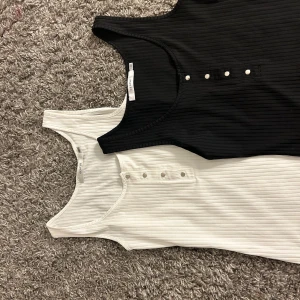 Två linnen i nyskick  - Två st linnen i svart och vitt, rubbat tyg vilket gör dem stretchiga. Snygga knappar som detalj över bysten Oanvända och nytvättade  Köp båda för 99kr eller ett för 69kr