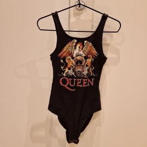 Queen body svart - Svart body med Queen motiv Obs är ett litet hål nära knäppningen men syns inte när man har byxor.