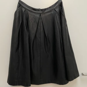 Skinnkjol  - Skinnskjol i fuskskinn (ser väldigt älta ut). Plisserad med fickor på sidan.   Strl: 38.  Köparen står för frakten.