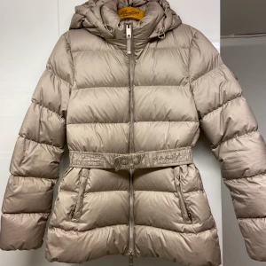 Nyskick dunjacka Massimo dutti - Som ny, använd fåtal gånger. Passar 34/36, jag är 165cm lång. Beige jacka med midjebälte som går att ta av, likaså med luvan💕