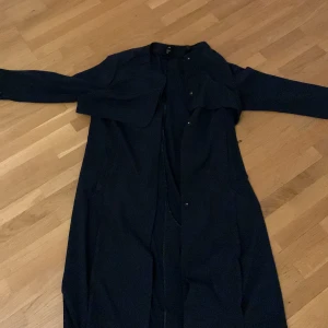 Lång mörkblå trench coat - Lång mörkblå trench coat, använts under en säsong, fortfarande i mycket gott skick. Elegant och stilren för en minimalistisk look. Har fickor 