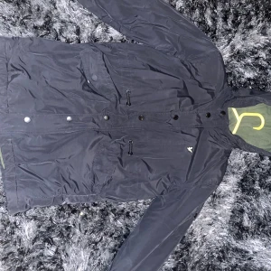 Lyle & ScottSVART OVERSIZED HEAVY PUFFA JACKET - Svart vadderad jacka från Lyle & Scott. Jackan har luva och jackmodellen är overzise. Framtill finns fickor med kardborre och märkets klassiska logga sitter på en patch och den är placerad på ena ärmen. Vårmeskalan på jackan är 3 av 4.   