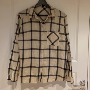Skjorta  - En beige rutig skjorta i storlek 38. Där rutorna går i svart och ljus ljus neongrön.Skjortan är i bra skick.Använd få gånger  