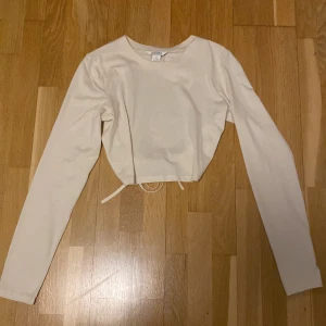 Open back crop top srl M - Beige långärmad croppad tröja med öppenrygg och knytning. Tröjan slutar lite över naveln. Säljer pga att jag aldrig använt den.