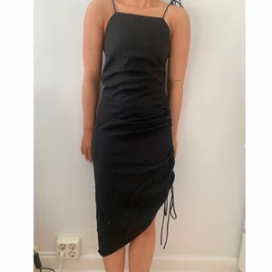 Svart Klänning med ”slits” - Svart Klänning från H&M i stl 34. Spagettistraps som går att reglera med knytning. Även ”slitsen” är reglerbar med knytning. Dragkedja och knäppe i sidan, inte stretchig i materialet. 