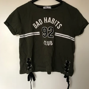 New Yorker FB Sister grön T-shirt stl S - Knappt använd grön T-shirt som är lite kortare! Tröjan är använd en gång och därför i väldigt fint skick! På slutet av ärmarna finns en vikning som är fastsydd. Längst ner på tröjan finns även två flätliknande knytningar på vardera sida!