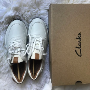 Clark Sneakers- White Combi Leather - Intressekoll på dessa supersnygga vita Clarks sneakers med bruna läderdetaljer. Helt nya, förpackningen kvar. Storlek 39. Kollar intresse och startar budgivning om det blir aktuellt. Köp direkt för 800kr, nypris ca 1100kr. Köparen står för frakten. Pris kan diskuteras!