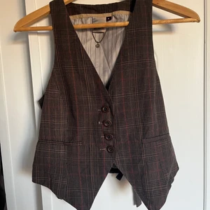 Retroväst - Assnygg populär väst i rutigt brunt mönster! Retro🤎 storleken är s men den är väldigt liten i storleken så skulle uppskatta till en xs! Den går dock att skjustera i ryggen!