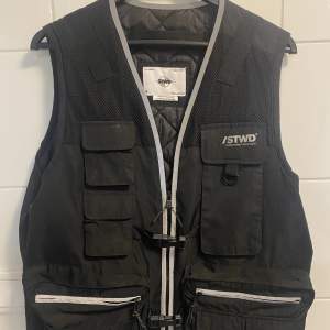 Tung väst från märket Mennace 💫  Perfekt väst för dig som diggar techwear eller gorpcore🫶🏻 Har reflexer så du syns bra när du är ute och går, så morsan inte behöver vara rädd 🤪  Knappt använd så har inga diffuser 🤝  Jag är 187 75kg, västen sitter truesize