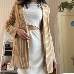 Sommar-Kavaj i linnetyg - En sommrig kavaj i linne-aktigt tyg. Randig i en fin gul/orange pastellfärg. Använd 1gång.   XS men passar S också