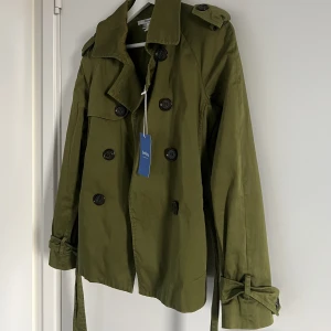 Vårjacka - Vårjacka köpt på Sellpy. Trenchcoat material. Lappen sitter kvar. Aldrig kommit till användning. Pris kan diskuteras. 