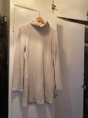 Stickad klänning med vida armar och hög krage  - Hög krage, visa armar och stickat. En underbar pudervit klänning. Helt oanvänd säljer på grund av flytt 