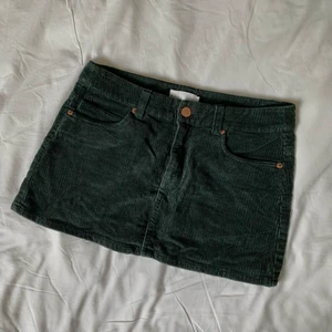 Minikjol i manchester 70’s stil - Jättesöt kortkort åtsittande kjol i mörkgrön manchester. Fem fickor, bakfickorna har så fina volangdetaljer! Storlek 34/xs