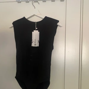 En festlig svart body m axelvaddar  - En svart festlig body m axelvaddar. Aldrig använd. 