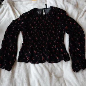 Blus från HM Divided - Svart blus med blommor. Smock upptill och något kjolaktigt nertill. Resår i ärmsluten och knäppning med knapp bak🥀 Använd en gång.