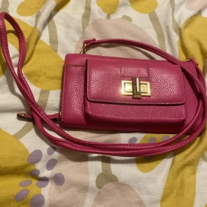 Väska - En ljus rosa handväska med en guld lås på framsidan helt ny aldrig andväns med råsa rep att bära väskan med kort hållare inne och konter om ni har frågor eller vill köpa så kan ni skriva eller ringa på 073500596 är mitt nummer ring om ni vill någont   