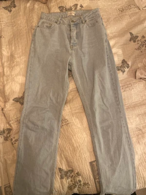 Blåa högmidjade jeans med slits  - Ett par blåa högmidjade jeans från na-kd,andvända några gånger,knappar istället för dragkedja 