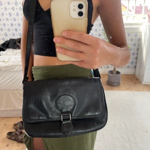 Svart väska - Svart väska köpt secondhand, sparsamt använd. Säljer då jag har för många väskor. Den är stor och rymlig med långa band som går att ha snett över kroppen. Väskan har en defekt som syns på sista bilden, personligen tycker jag bara det gör väskan snyggare.