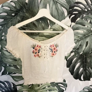 off shoulder topp vit blommig - En vit offshoulder topp med fina blommor på! Köpt på hollister och i fint skick. Insydd i ryggen men det är bara att sprätta upp om en inte vill ha det. S och M