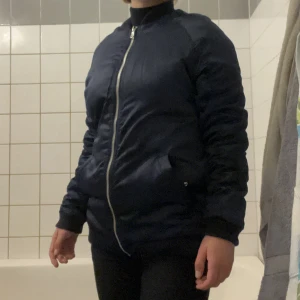 Blå bomberjacka med tryck - Typ aldrig använd! Lite längre i modellen men går att vika in där nere. Väldigt mjuk/lite glansig med ett stort tryck på ryggen