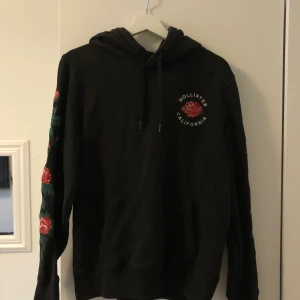 hoodie från hollister - mörkgrå hoodie med rosor på ärmar och på framsidan. storlek S 🤍