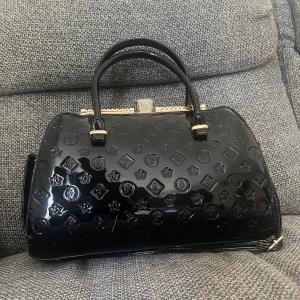 Svart väska  - Snygg svart väska, vet ej tror den är gjord av plast typ, men mycket fint skick och gott med utrymme, finns även extra långa band till den. Den är köpt för drygt 600kr 