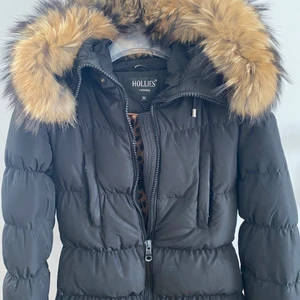 Hollies jacka - En fin svart dunjacka från hollies med pälskrage i storlek 34. Leopardfärgat foder, muddar i ärmslut, fickor vid bröstet. Två små knappar har lossnat på pälskragen med det är lätt att fixa! Varm och skön, fint skick! 