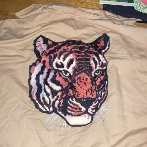 Beige overshirt från Lager 157 som jag sytt fast en tiger på samt ett annat silvrigt märke. Storleken är s-m.