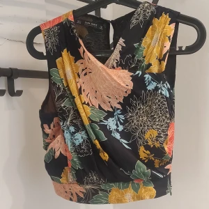 Croppad blommig top från Zara i fantastiskt mönster! - Materiallapp bortklippt men yttertyg med lite lyster och tunnt mjukt innertyg.  Sparsamt använd och i gott skick. Säljes då den är lite för liten 