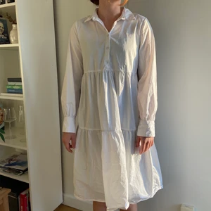 NA-KD sommarklänning  - En vit långärmad klänning från NA-KD i strl 34. Har en knäppning vid bysten samt knappar vid ärmslutet! Den faller lite längre i bak vilket är fint! Jag har använt den ett fåtal gånger, så i stort sett oanvänd! Kan skickas om så önskas, fraktkostnad ti