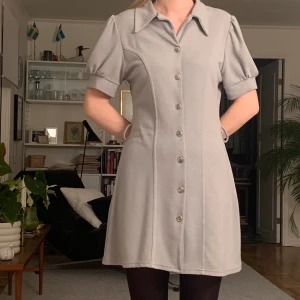 Grå trikåklänning st M  - Mjuk trikåklänning i grått tyg. Färgen är mer likt ljusblå i verkligheten. Vintage stil med krage, knäppning och puffiga ärmar. Kommer med ett bälte också, men funkar lika bra utan. Köpt på second hand, men knappt använd och har inga tydliga märken på slitage. 85% polyester, 10% nylon, 5% elastane. 