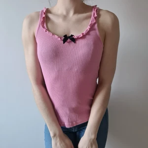 Rosa linne med volanger och svart rosett - Rosa ribbat linne med volang i urringningen och en svart rosett. Gullig topp av märket Floozie (Frost French), size 8 (passar XS-S).