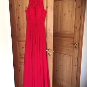 Lilly röd balklänning stl 36 - Lilly röd balklänning med blommig spets uptill. Klänningen har inbyggd bh och är bara använd en gång.